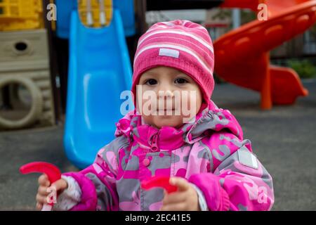 Kleines Kleinkind in warmen Winteroveralls spielt auf dem Spielplatz. Weicher Fokus Stockfoto