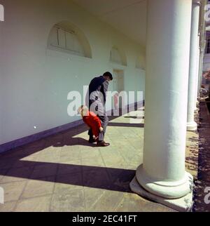 Präsident Kennedy mit John F. Kennedy, Jr. (JFK, Jr.), u0026 Caroline Kennedy (CBK). Präsident John F. Kennedy spielt mit seiner Tochter Caroline Kennedy (die zwischen ihren fatheru2019s Beinen läuft) in der West Wing Colonnade des Weißen Hauses, Washington, D.C., John F. Kennedy, Jr., steht im Hintergrund vor der Tür. Stockfoto