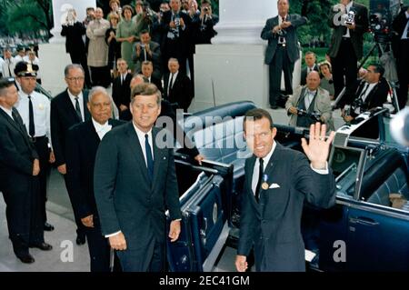 Präsentation der National Aeronautics and Space Administration (NASA) Distinguished Service Medal (DSM) an Astronaut Major L. Gordon Cooper, 12:15pm Uhr. Astronaut Major L. Gordon Cooper (rechts) winkt zu Zuschauern, bevor er in die Präsidentenlimousine (Lincoln-Mercury Continental Cabrio) tritt, nach seiner Abreise aus dem Weißen Haus nach seiner Zeremonie zur Verleihung der Distinguished Service Medal (DSM) der National Aeronautics and Space Administration (NASA). Präsident John F. Kennedy steht auf der linken Seite. Ebenfalls im Bild: Senator Clinton P. Anderson (New Mexico), Vorsitzender des Senats Aeronautic Stockfoto