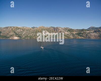 Luftaufnahme von einer Drohne - die Yacht segelt in den Gewässern der Bucht von Kotor vor der Kulisse der Berge und blauen Himmel von Montenegro. Stockfoto