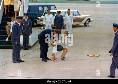 Wochenende im Hyannis Port: Präsident Kennedy mit Caroline Kennedy (CBK) und John F. Kennedy, Jr. (JFK Jr.), auf der Otis Air Force Base. Präsident John F. Kennedy (links, mit Hut) begrüßt seinen Sohn John F. Kennedy, Jr., bei seiner Ankunft auf der Otis Air Force Base, Cape Cod, Massachusetts. Caroline Kennedy (von der Kamera weggewandt) steht rechts von Präsident Kennedy und John, Jr; United States Air Force Lieutenant Thomas O. Johnson steht im Zentrum der Gruppe vor dem Auto im Hintergrund. Alle anderen sind nicht identifiziert. Stockfoto