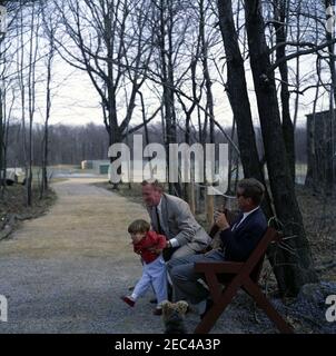 Wochenende im Camp David. Präsident John F. Kennedy (rechts, hält Pfeife und trägt Sonnenbrille) sieht an, wie Kennedy-Familienfreund und Untersekretär der Marine, Paul u0022Redu0022 Fay, John F. Kennedy, Jr. Kennedy-Familienhund, u0022Charlie,u0022 sitzt links von Präsident Kennedy. Camp David, Frederick County, Maryland. Stockfoto