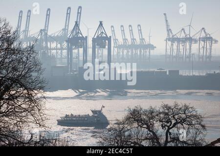 Hamburg, Deutschland. Februar 2021, 13th. Eine Fähre fährt stromaufwärts durch die teilweise gefrorene Elbe. Im Hintergrund sind die Kraniche im Hamburger Hafen zu sehen. Quelle: Georg Wendt/dpa/Alamy Live News Stockfoto