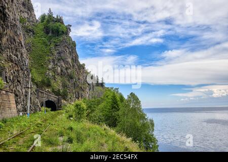 Eine alte Eisenbahn am Rande des Baikalsees. Das Portal des Tunnels unter der hohen Klippe. Der Weg ist mit grünem Gras bewachsen. Region Irkutsk. Osten Stockfoto