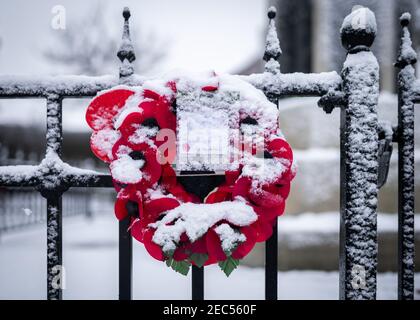 Remembrance Day roter Mohnblütenkranz, der an schwarzen Geländern befestigt ist Am Sonntag den 11th. November im Schnee Winterszene Stockfoto