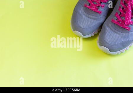 Sportschuhe grau mit leuchtend rosa Schnürsenkeln auf hellgelb Hintergrund, gesunder Lebensstil, Platz für Text Stockfoto