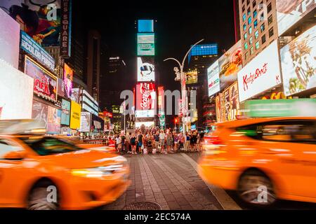 Verkehr am Times Square in der Nacht mit verschwommenen Taxis Bewegung und Menschen, die die Straße überqueren Stockfoto