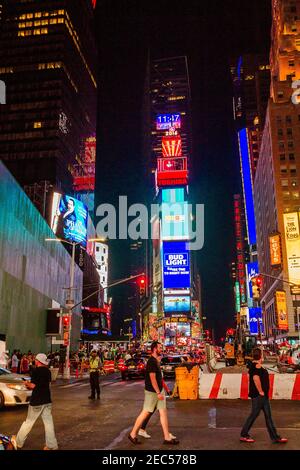 Nachtansicht des Times Square mit drei Personen, die die Straße überqueren Und Traffic-Agent, der den Datenverkehr verwaltet Stockfoto