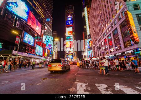 Nachtverkehr am Times Square mit vielen Touristen, Taxis und Autos und einem Verkehrsagenten, der die Straße überquert Stockfoto