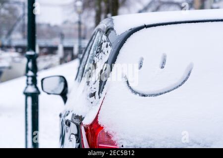 Geparktes Auto im Winter mit Schnee bedeckt mit einem Smiley-Gesicht Emoji auf der Heckscheibe des Autos auf der Straße gezeichnet. Stockfoto