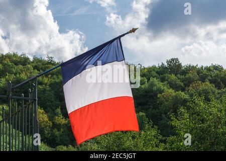 Französische Flagge winkt im Wind auf Balkon Fahnenmast gegen grüne Bäume Landschaft und Himmel mit Wolken an sonnigen Tag, Nahaufnahme Stockfoto