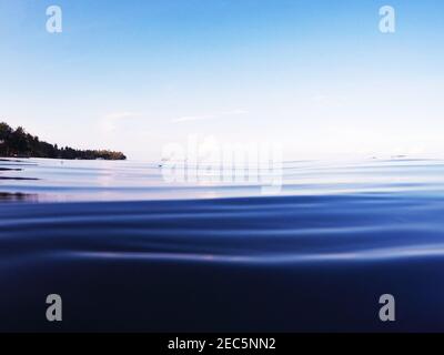 Meereswasseroberfläche mit gewelltem Wasser und entfernter Küste. Tropische Natur nach Sonnenuntergang getönte Foto. Dunkles Meerwasser und heller Himmel. Minimales Banner am Meer Stockfoto