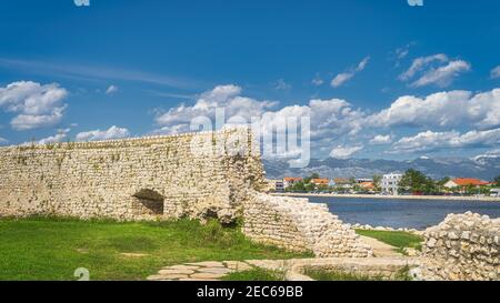 Zerstörte Mauer oder Festung, die Nin Dorf mit Blick auf moderne Bezirk und Gebirge der Dinarischen Alpen umgeben war der Hintergrund, Kroatien Stockfoto