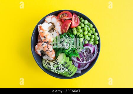 Poke Schüssel mit roten Garnelen und Gemüse in die dunkle Schüssel in der Mitte des gelben Hintergrunds.Draufsicht.Nahaufnahme. Stockfoto