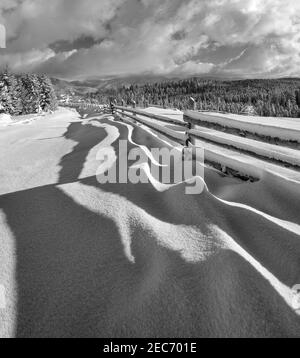Graustufen. Malerisch gewellte Schatten auf Schnee vom Holzzaun. Alpine Berg Winter Weiler Stadtrand, verschneiten Weg, Tannenwald. Hochauflösendes Bild w Stockfoto