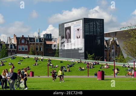 Menschen entspannen auf einem grünen Feld vor dem Stedelijk Museum Amsterdam, Niederlande. Plakatwand des Stedelijk Museums. Stockfoto