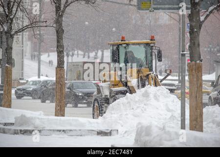 Moskau, Russland, 13. Februar 2021: Ein gelber Traktor räumt nach Schneefall und Niederschlägen verschneite Straßen in einer Stadtstraße. Stockfoto