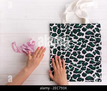Womans Hände wählen Öko Einkaufstasche mit trendigen Leopardenmuster Druck gegen eine Plastiktüte auf weißem Holzhintergrund, Flat Lay, Top View. Plan speichern Stockfoto