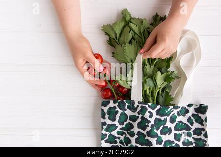 Hände einer Frau nehmen frische Bio-Tomaten aus dem Eco Shopping Bag mit trendigem Leopardenmuster-Print auf Holzhintergrund, Flat Lay. Draufsicht. Eco Stockfoto