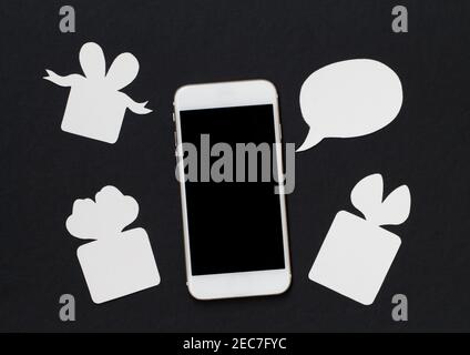 Weißes Telefon mit Textblase und Geschenkbox auf schwarzem Hintergrund. Schwarz-Weiß-Banner-Vorlage mit Textplatz. Smartphone und Gegenwart. Schwarzer Bildschirm c Stockfoto