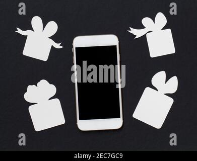 Weißes Telefon mit Geschenkboxen auf schwarzem Hintergrund. Schwarz-weiße Bannervorlage mit Smartphone und Papier schneiden Geschenke. Schwarzer Bildschirm Handy flach l Stockfoto