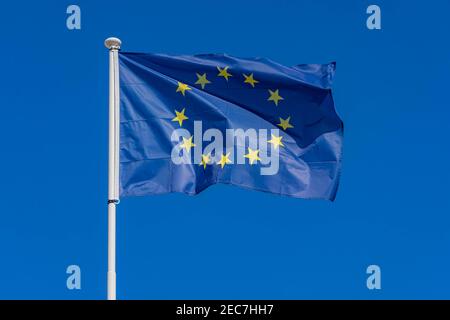 Einzelne europäische Flagge mit zwölf gelben Sternen winken im Wind auf blauem Himmel Hintergrund, Nahaufnahme. EU-Flagge Stockfoto