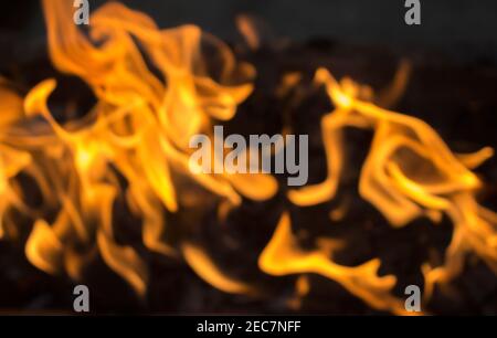 Gelbes Feuer auf fehlende Kohle. Abstraktes, unscharrides Foto für den Hintergrund. Verschwommene Kamintapete. Vorlage für Banner mit brennendem Feuer. Glänzende Flamme des Lagerfeuers Stockfoto