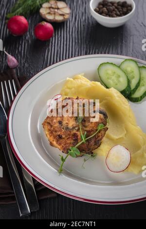 Hackfleischschnitzel mit Kartoffelpüree auf weißem Teller auf schwarzem Holzhintergrund. Draufsicht, flach liegend Stockfoto