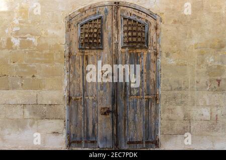 Vintage alten Lagerhaus Holz braun bemalte Tür mit alten Backstein Wand aus Kalkstein. Vorderansicht der Tore zum verlassenen Lagerhaus in Malta Stockfoto