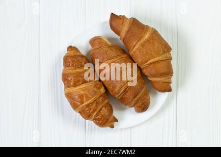 Teller mit frisch gebackenen Croissants auf weißer Holzplatte Anzeigen Stockfoto