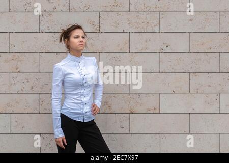 Attraktive Frau in weißem Hemd stehen auf Marmor Backstein Wand Hintergrund und Blick nach vorne. Erfolgreiches und zielgerichtliches Frauenkonzept. Speicherplatz kopieren. Stockfoto