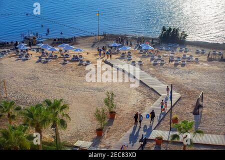 Menschen, die am Strand des Crowne Plaza Dead Sea Hotels im Toten Meer, Jordanien, schweben und mit schwarzem Schlamm aus dem Toten Meer bedeckt sind. Stockfoto