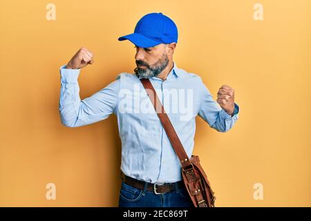 Mann mittleren Alters mit Bart und grauen Haaren trägt Lieferung Kurier Kappe zeigt Arme Muskeln lächelnd stolz. Fitness-Konzept. Stockfoto