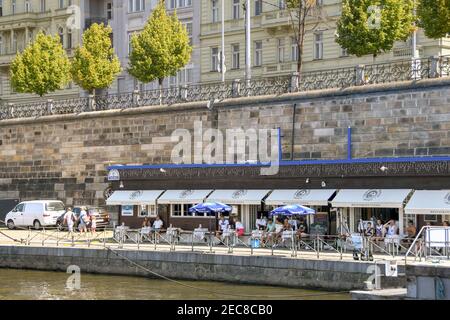 Prag, Tschechische Republik - Juli 2018: Menschen, die vor einem Café am Flussufer am Ufer der Moldau in Prag sitzen Stockfoto