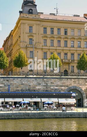 Prag, Tschechische Republik - Juli 2018: Menschen, die vor einem Café am Flussufer am Ufer der Moldau in Prag sitzen Stockfoto