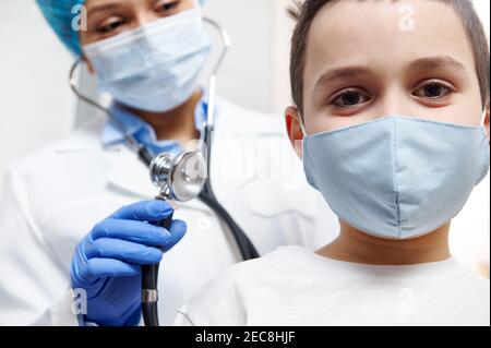 Lächelnder Junge in medizinischer Schutzmaske während der Untersuchung eines Kinderarztes Stockfoto