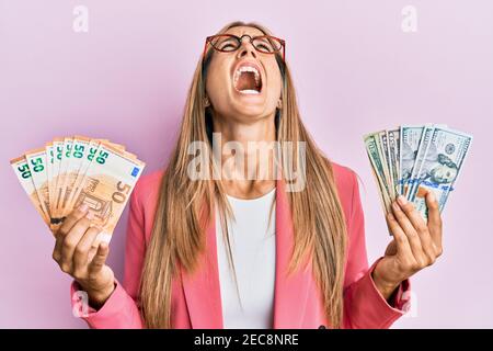 Junge blonde Frau im Geschäftsstil hält Dollar und Euro-Banknoten wütend und verrückt schreien frustriert und wütend, schreien mit Wut Blick Stockfoto