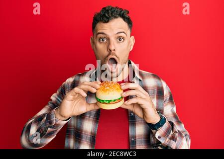 Junge hispanic Mann essen einen leckeren klassischen Burger Angst und schockiert mit Überraschung und erstaunt Ausdruck, Angst und aufgeregt Gesicht. Stockfoto