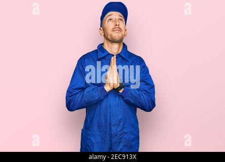Glatze Mann mit Bart tragen Baumeister Jumpsuit Uniform Betteln und beten mit Händen zusammen mit Hoffnung Ausdruck auf Gesicht sehr emotional und besorgt. Stockfoto