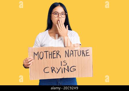 Junge schöne asiatische Mädchen hält Mutter Natur weint Protest Karton Banner Abdeckung Mund mit Hand, schockiert und Angst vor Fehler. Überraschung Stockfoto