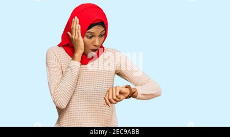 Junge afroamerikanische Frau trägt traditionelle islamische Hijab Schal Blick auf die Uhr Zeit besorgt, Angst, zu spät Stockfoto