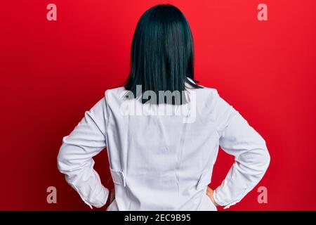 Junge hispanische Frau trägt Ärztin Uniform und Stethoskop rückwärts stehend Wegschauen mit Armen am Körper Stockfoto