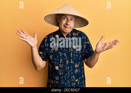 Mittelalter kahler Mann trägt traditionelle asiatische Strohhut ahnungslos und verwirrt mit offenen Armen, keine Ahnung und zweifelhaftes Gesicht. Stockfoto