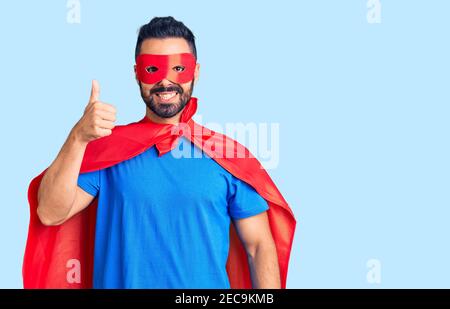 Junger hispanischer Mann trägt Superhelden Kostüm lächelnd glücklich und positiv, Daumen nach oben tun hervorragende und Zustimmung Zeichen Stockfoto