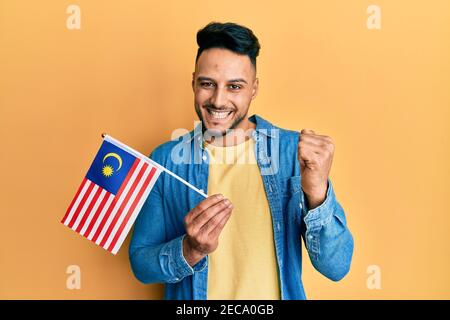 Junger araber hält malaysia Flagge schreien stolz, feiert Sieg und Erfolg sehr aufgeregt mit erhobenem Arm Stockfoto