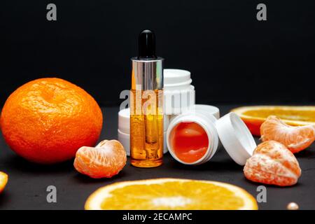 Vitamin C Gesichtspflege Kosmetik-Konzept - Bio-Serum in einer Flasche und Creme mit natürlichen Inhaltsstoffen. Mandarinen- und Orangenscheiben. Stockfoto