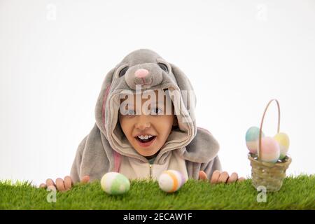 Mädchen im Hase Kostüm Blick auf Osterei auf grünem Gras. Isoliert auf weiß. osterfeiertagskonzept Stockfoto