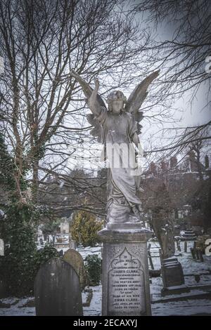 Ein Grabstein mit einer Engelsstatue auf dem Hampstead Friedhof, Schnee, Grabsteine, Gräber, Winterwetter Stockfoto