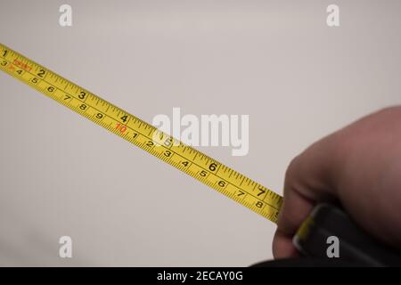 Hand hält ein gelbes Maßband auf weißem Hintergrund. Handmessung mit Klebeband. Stockfoto