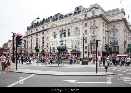 Menschen, die um den Shaftesbury Memorial Fountain im Picadilly Circus mit dem Criterion Theatre dahinter sitzen, London England Großbritannien Stockfoto